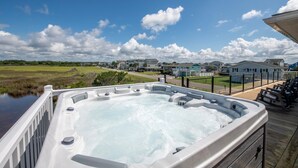 A hot tub on a wooden deck with a view of houses and a marshy landscape.