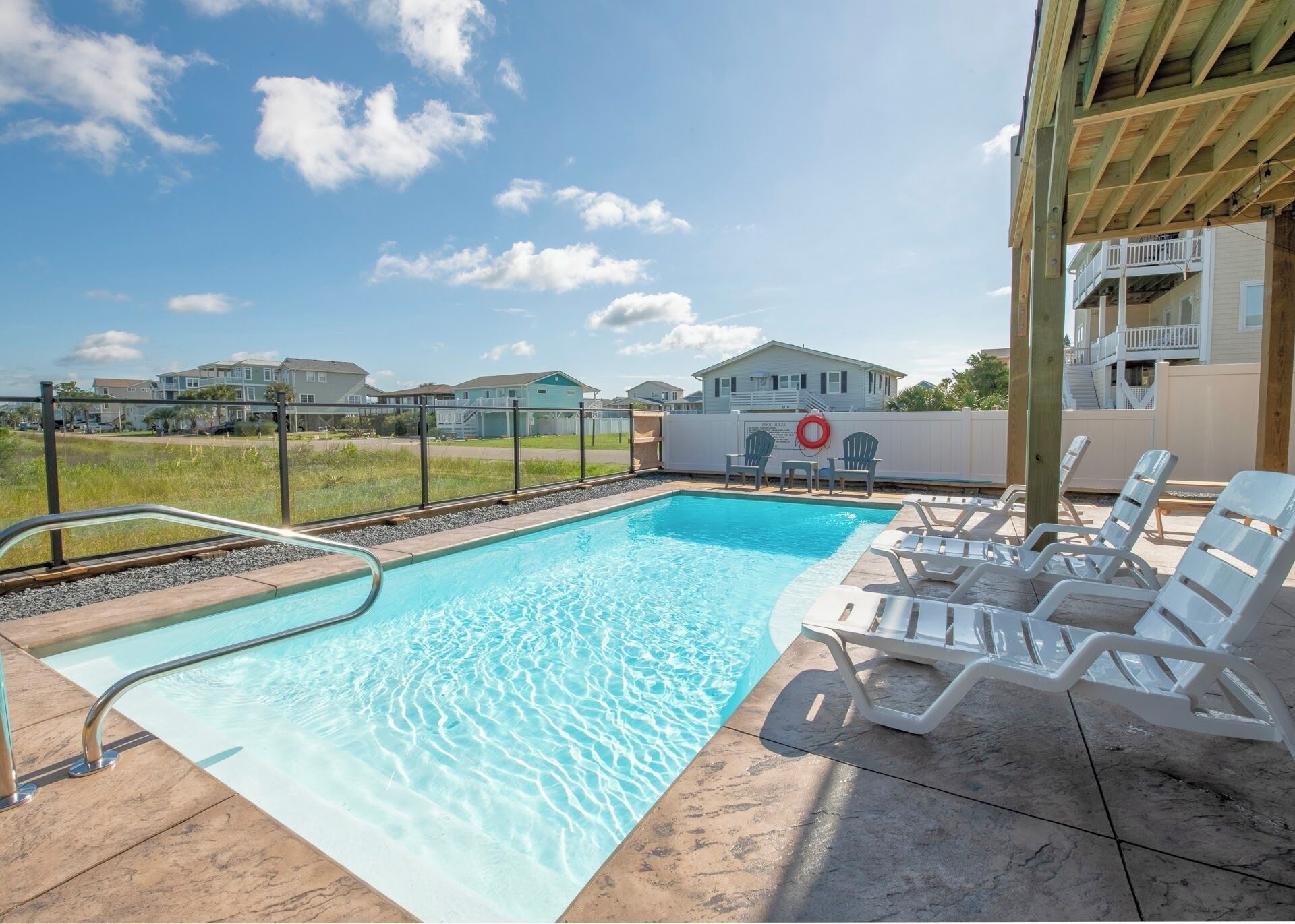 A swimming pool with a clear blue water, surrounded by lounge chairs and a wooden deck.