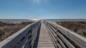 A wooden boardwalk leading to a beach with a clear sky and sun shining.
