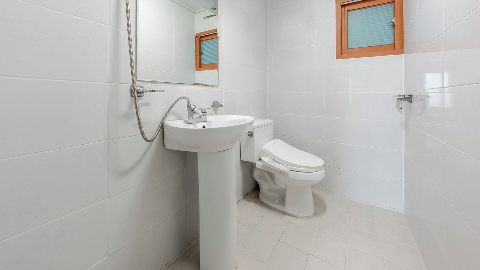 A bathroom with white tiles, a white sink, a toilet, and a shower.