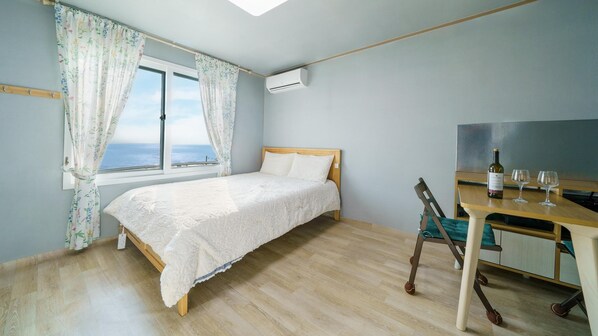 A bedroom with a bed, a window with curtains, a desk with a chair, a bottle of wine, and glasses.