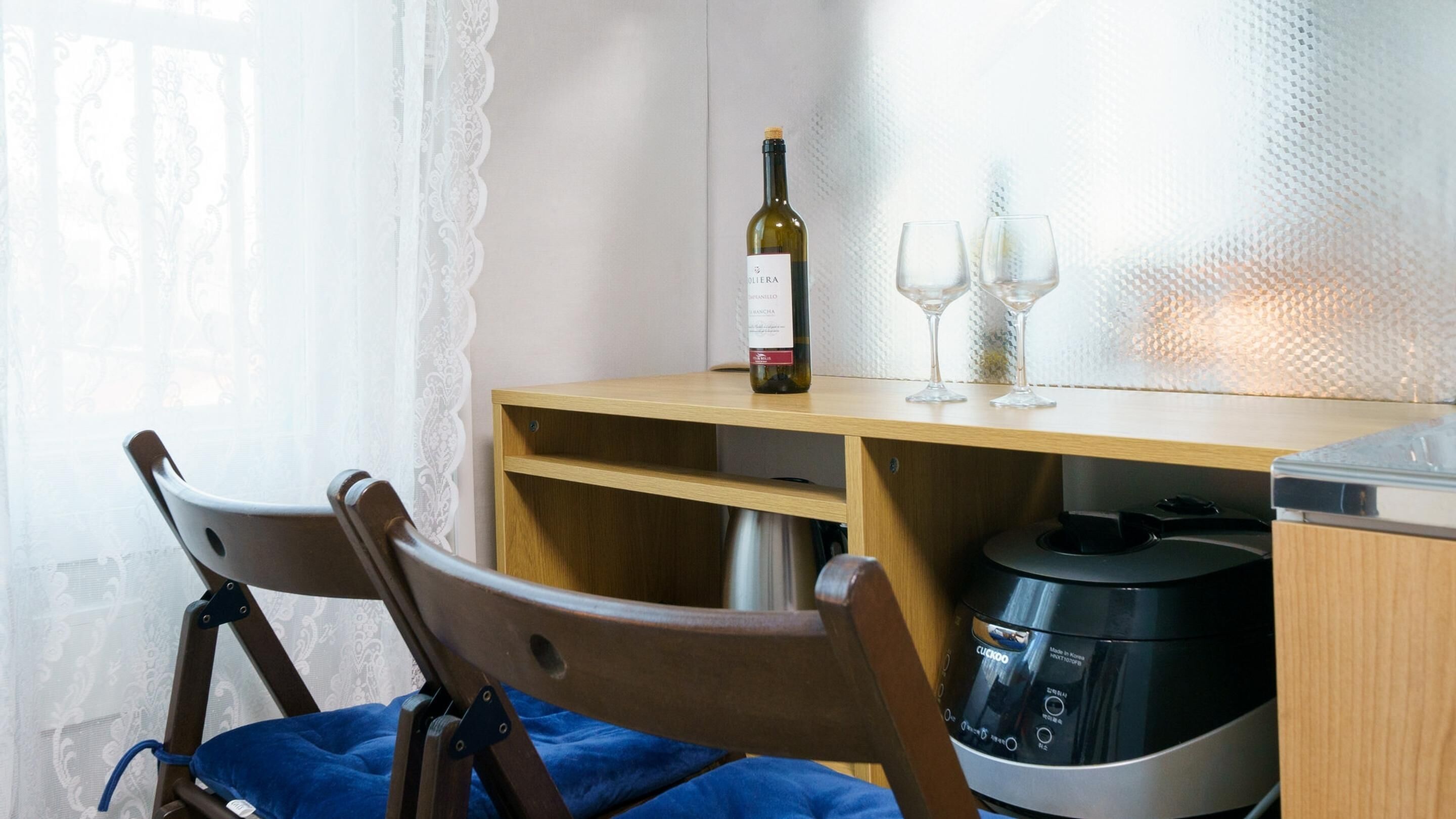 A kitchen area with a wooden table, a wine bottle, two wine glasses, a chair, and a coffee maker.