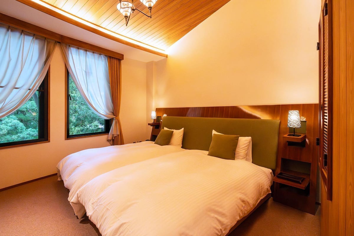 Ein Hotelzimmer mit einem großen Bett, zwei Vorhängen, einer Holzbalkendecke und einem Nachttisch mit Lampe.