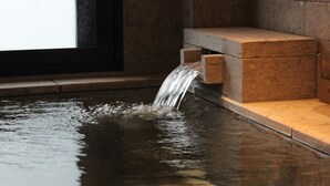 A water feature with a stream flowing into a pool, set against a stone wall. - NIKKO-NISHIMACHICLUB A LA TOUTO (Nikko)