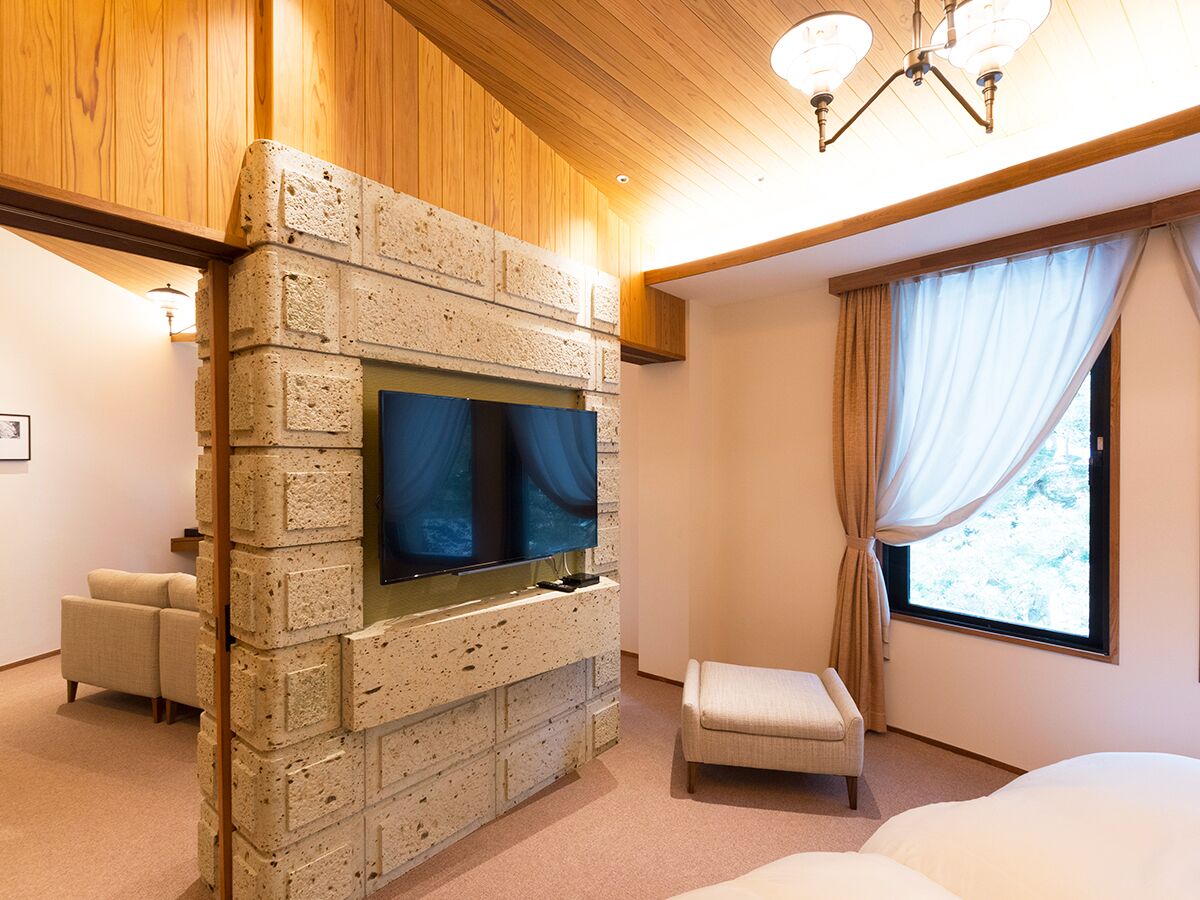 A bedroom with a stone wall, a TV, a window with curtains, and a bed.