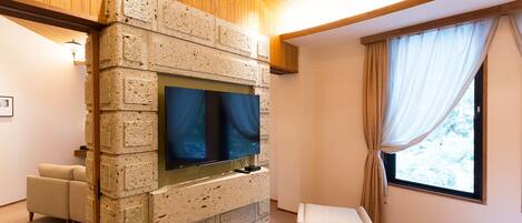 A bedroom with a stone wall, a TV, a window with curtains, and a bed.