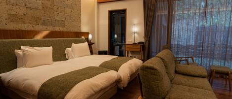 A hotel room with a large bed, a sofa, a desk, and a window with curtains.