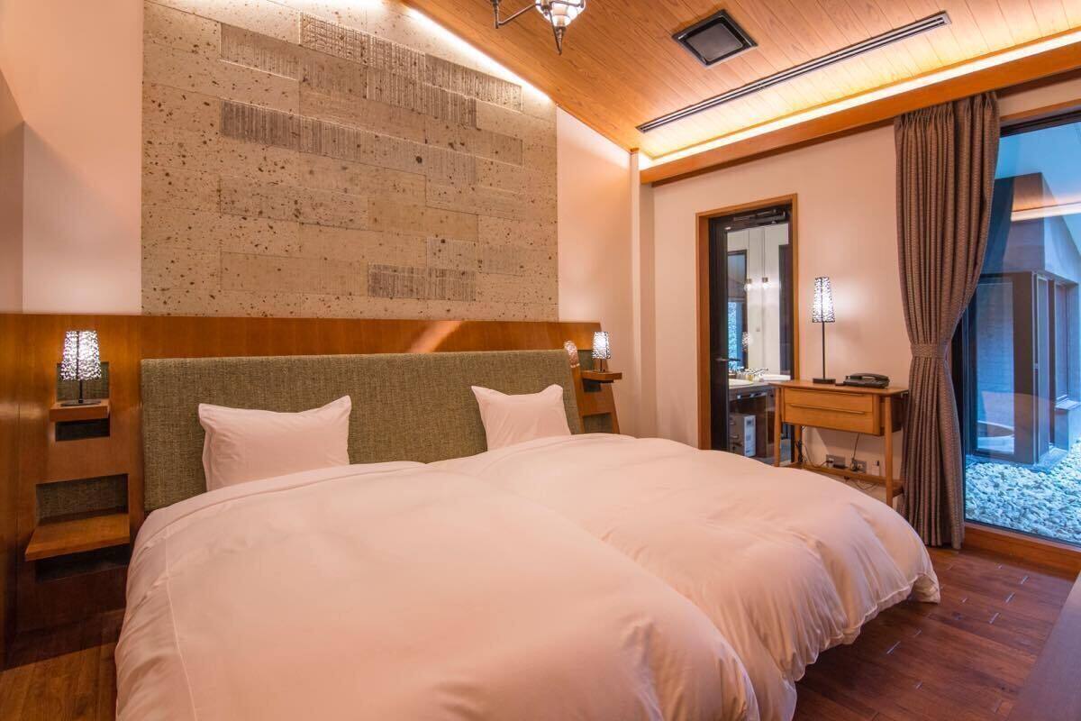 A hotel room with a large bed, a wooden headboard, a wall with a textured pattern, a mirror, a desk, and a view of a snowy outdoor area.
