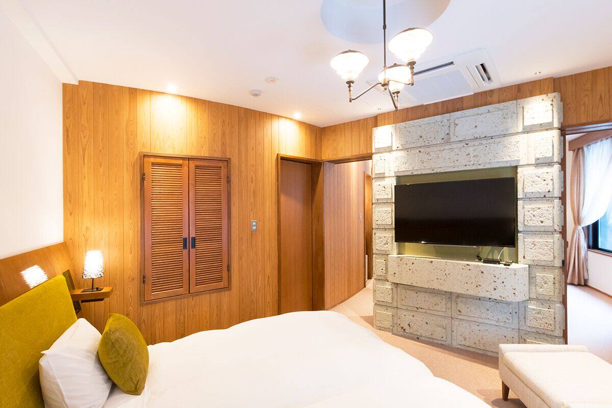 A hotel room with a large bed, wooden panel walls, a stone fireplace, and a flat-screen TV mounted on the wall.
