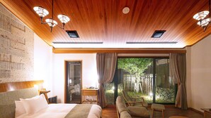 A hotel room with a large bed, a sofa, a small table, and a view of a garden through a glass door. - NIKKO-NISHIMACHICLUB A LA TOUTO (Nikko)
