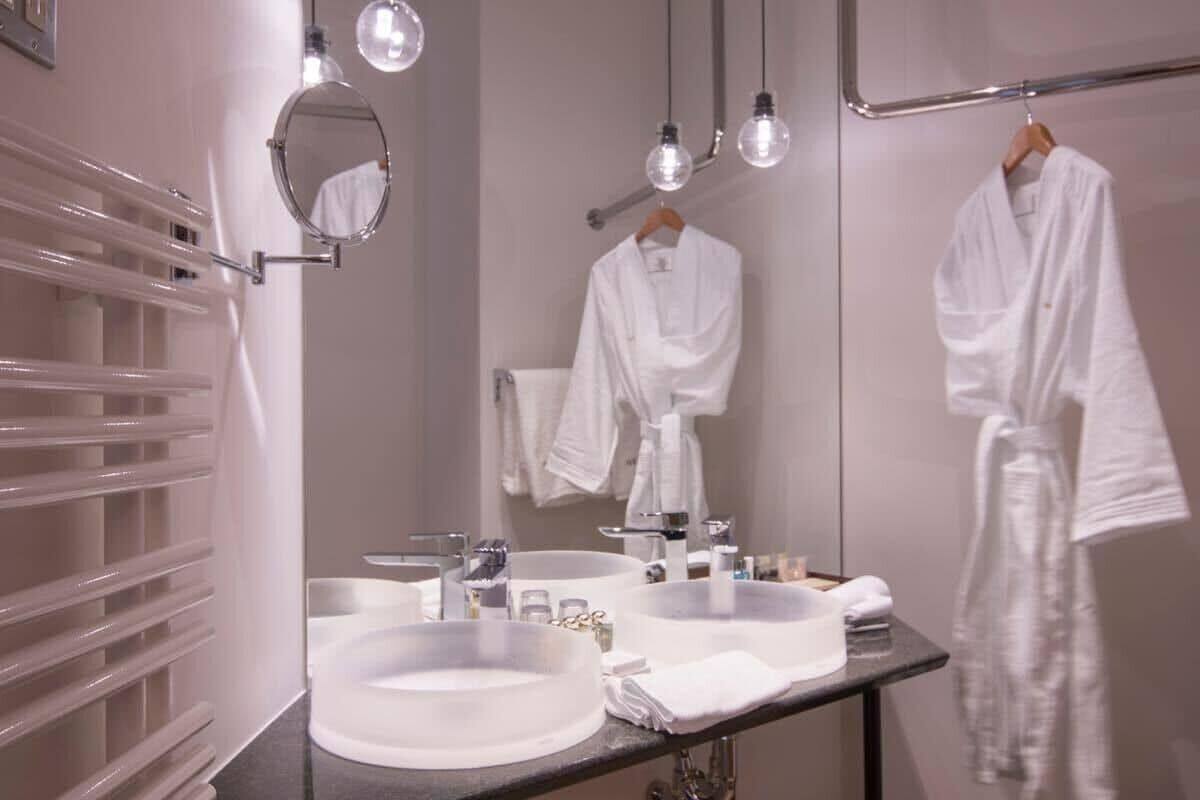 A bathroom with two sinks, a mirror, and a towel rack with white robes.