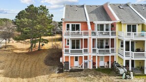 A multi-story residential building with balconies, a driveway, and a sandy area with trees. - Sandy Paws Townhouse, Private Mini Water Park, Dog Friendly! (Kill Devil Hills)
