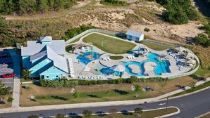 An aerial view of a resort with a large pool area, a tennis court, and a building with a blue roof. - Sandy Paws Townhouse, Private Mini Water Park, Dog Friendly! (Kill Devil Hills)