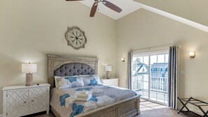 Ein Schlafzimmer mit einem großen Bett, zwei Nachttischen, einem Deckenventilator, einem Wanddekor und Blick ins Freie durch eine Schiebetür.