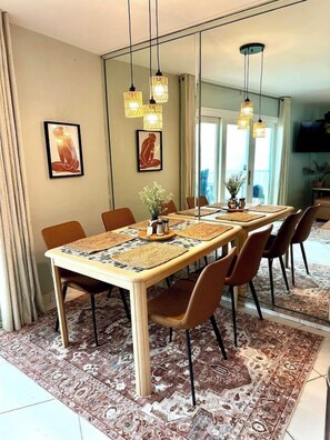 A dining area with a long table, chairs, hanging lights, and artwork on the walls.