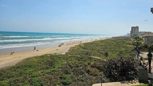 A beach with a view of the ocean, a few people, and a building in the background. - Amazing Beachfront view and access! Pool & hot tub (South Padre Island)