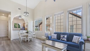 A spacious living room with a blue sofa, a wooden coffee table, and a dining area with white chairs and a white table. - Lake & Mountain View Condo - The Cliffs on Indian Point - Silver Dollar City (Branson)