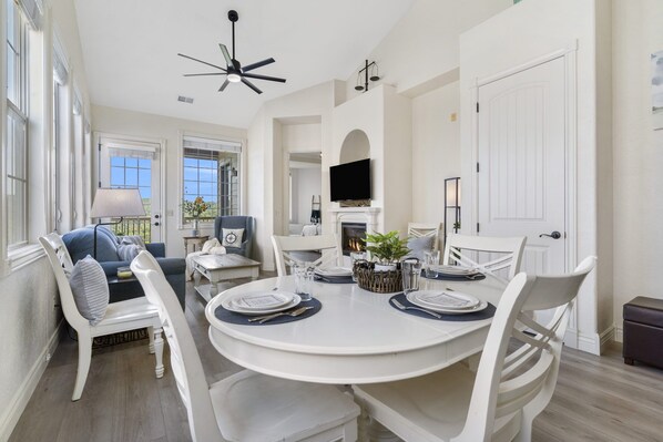 A dining area with a round table set for four, white chairs, a fireplace, and a television mounted above it.