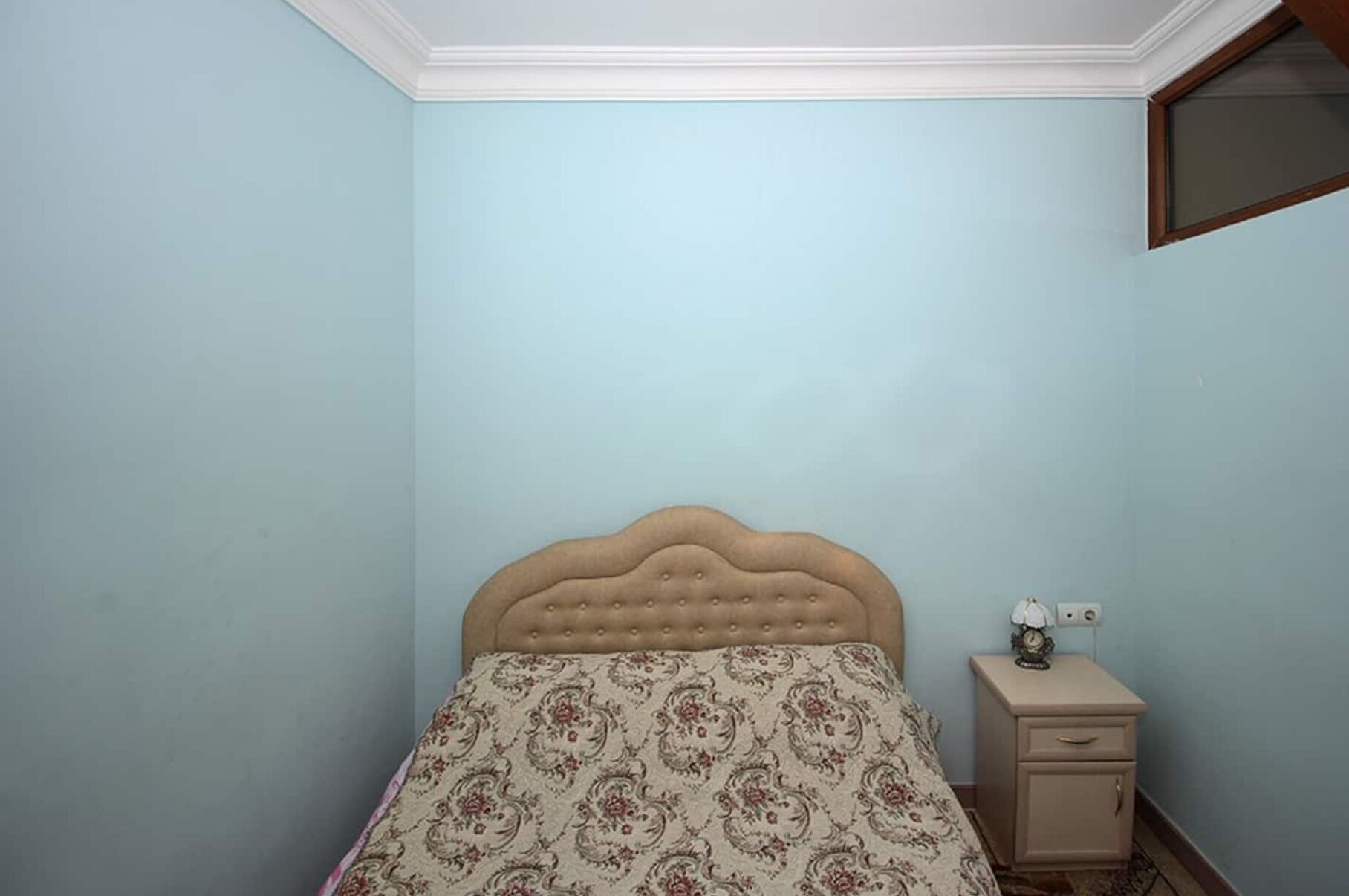 A bedroom with a single bed, a nightstand, and a wall-mounted mirror.