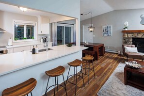 A modern kitchen with a large island, wooden stools, and a dining area with a fireplace.