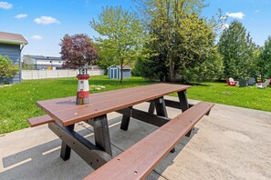 Ein Picknicktisch mit Bänken, eine kleine Dekoration, eine Rasenfläche mit Bäumen und einem Zaun.