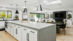 A modern kitchen with a large island, pendant lights, and a flat-screen TV. - SWSS 7BR Estate | Golf Sim | Sauna | Pool | Hot Tub | Putting Green | Volleyball | Games (Scottsdale)