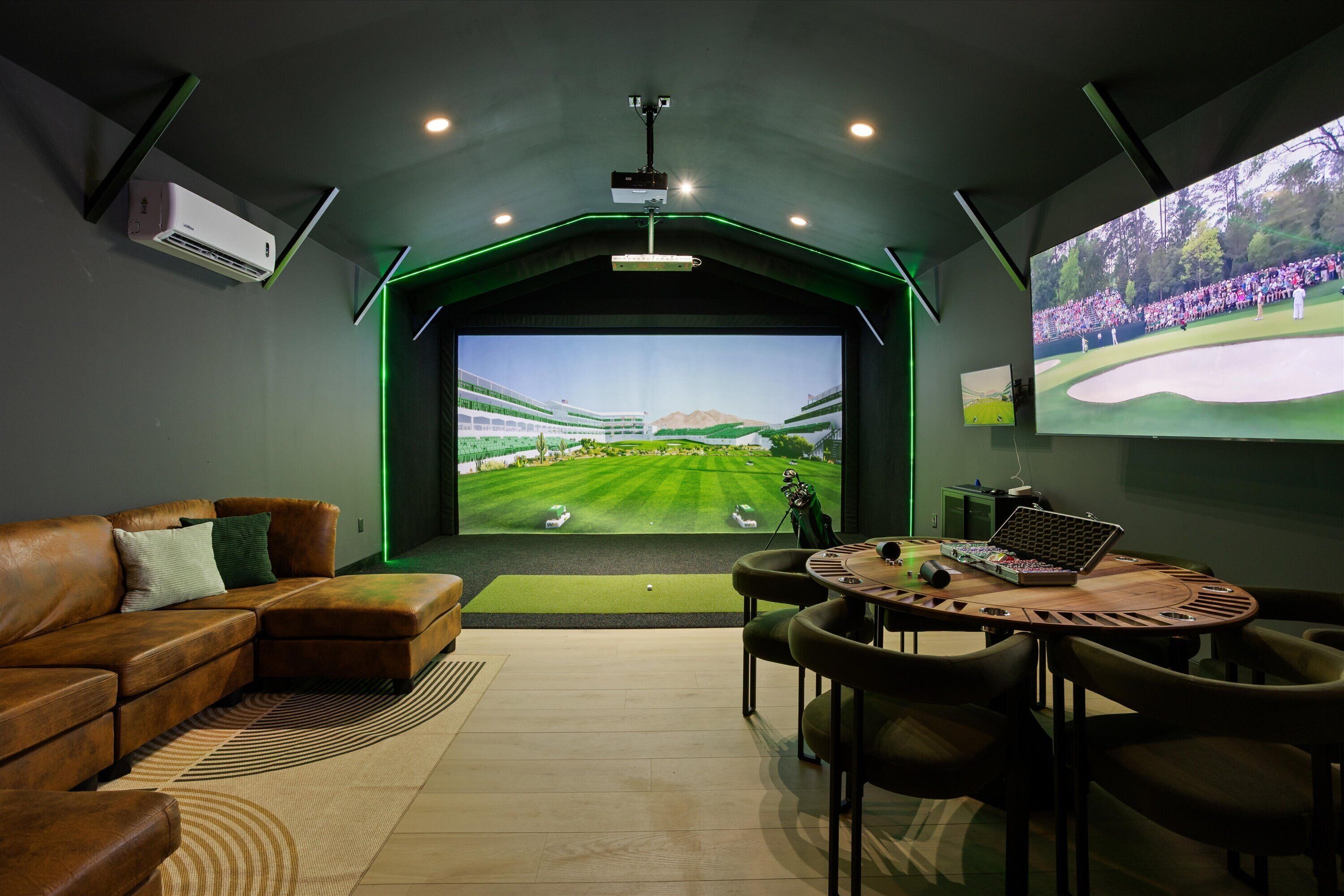 A room with a large screen displaying a golf course, a brown leather sofa, a round wooden table, and a projector mounted on the ceiling.