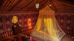 Ein Zimmer mit einem Himmelsbett, einem Schminktisch, einem Spiegel und Wandverkleidung mit Muster.
