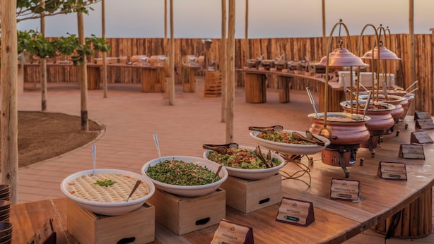 Ein reichhaltiges Buffet mit verschiedenen Speisen und Namensschildern, Holztische und eine Pergola-Struktur.