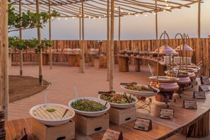Een buffetopstelling met diverse gerechten en naambordjes, houten tafels en een pergola.
