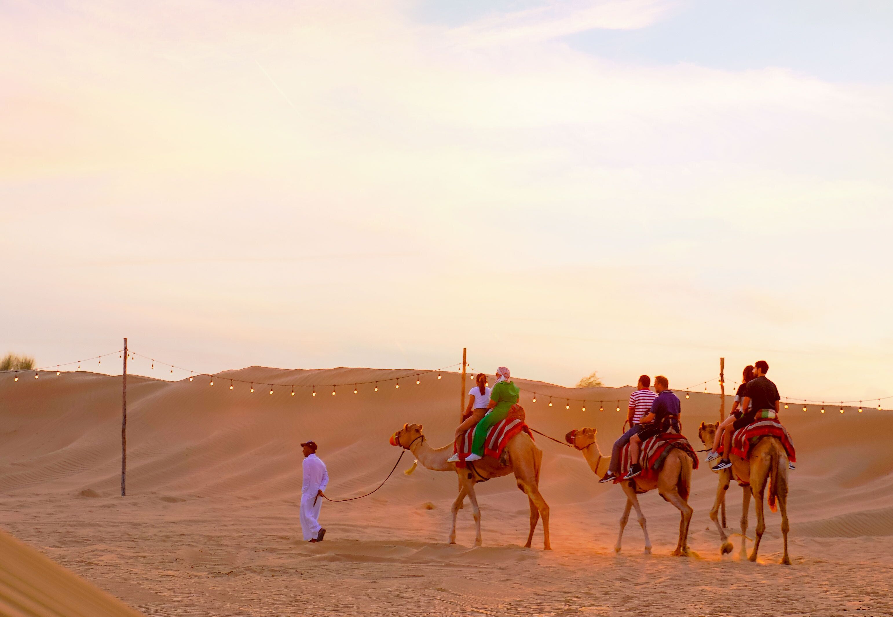 A desert scene with camels and people riding them.