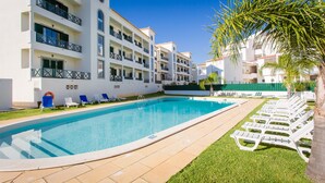 A poolside area with a clear blue pool, white lounge chairs, and a building with balconies. - Central Albufeira 2-B Apt, Sleeps 6, Pool, Parking (Albufeira)