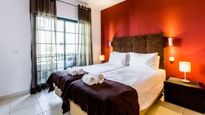 A hotel room with a large bed, two bedside tables, a window with curtains, and a view of the outside. - Central Albufeira 2-B Apt, Sleeps 6, Pool, Parking (Albufeira)