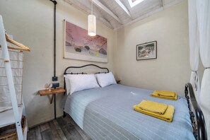 A bedroom with a bed, pillows, a bedside table, a hanging light fixture, a framed picture on the wall, and a window with curtains. - Little Linney - Sleeps 2 - Garden - Parking - Wifi (Bideford)