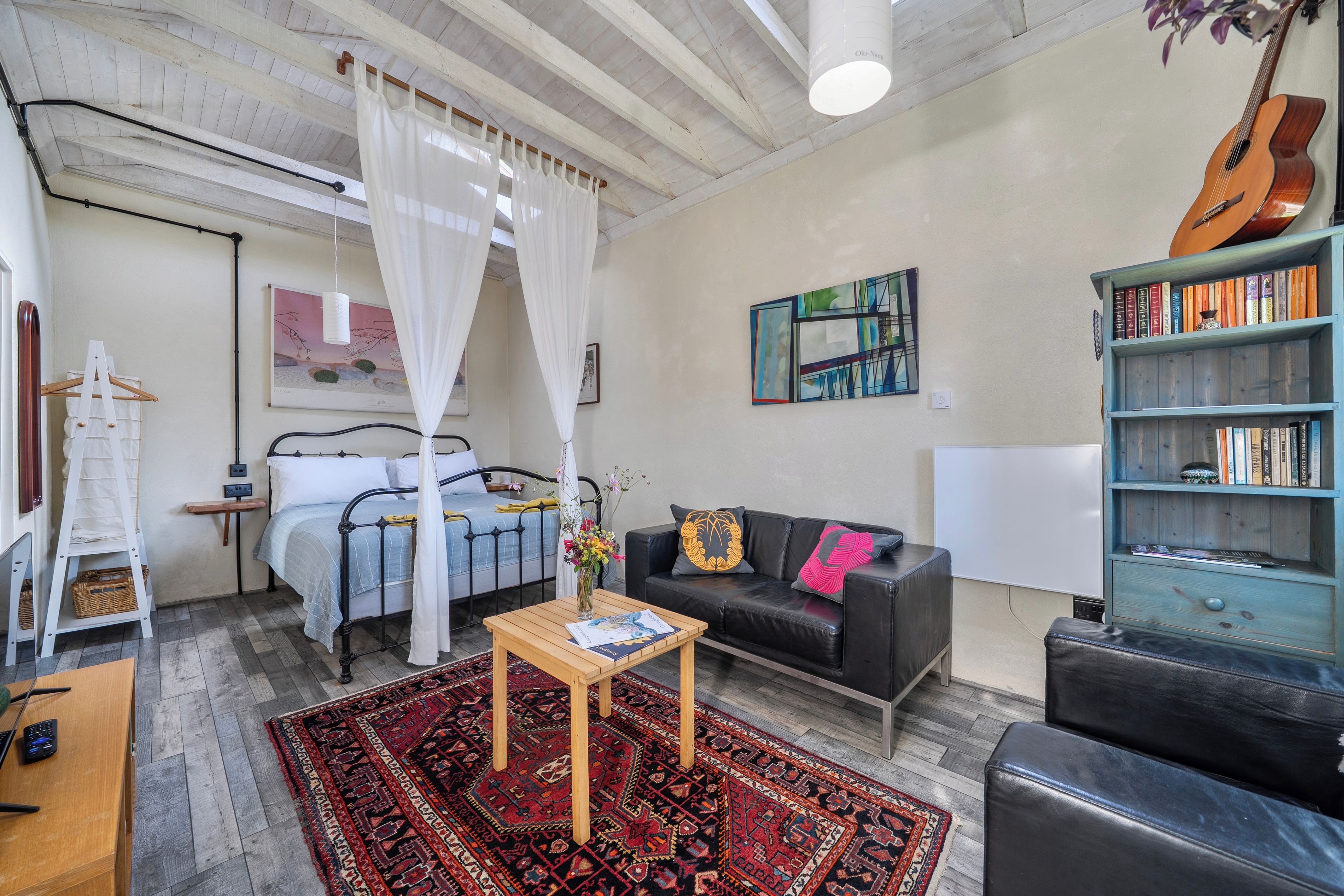 A room with a bed, a black sofa, a coffee table, a bookshelf, and a guitar.