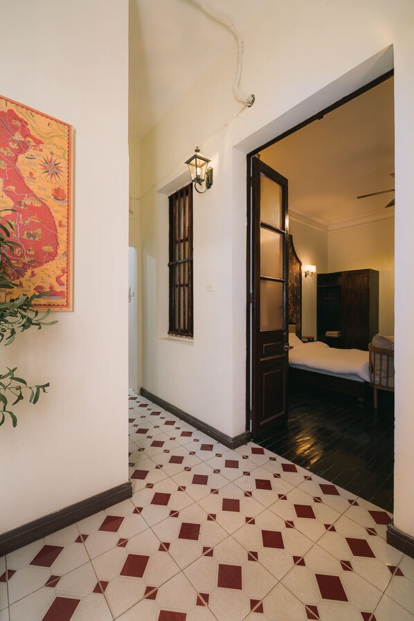 A hallway with a tiled floor, a door leading to a bedroom, and a wall-mounted light fixture.