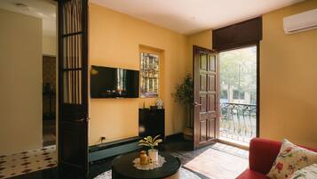 A living room with a television, a sofa, a small table with a plant, and a door leading to an outdoor balcony.