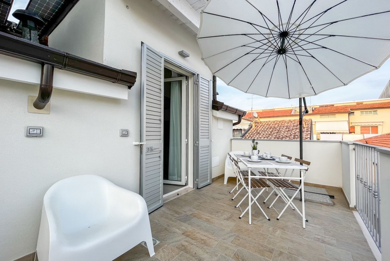 Ein Balkon mit einem weißen Tisch, Stühlen und einem Sonnenschirm.