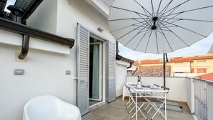 Un balcón con una mesa y sillas blancas, una sombrilla y una silla blanca.