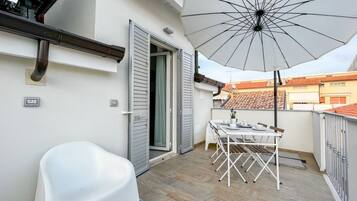 Ein Balkon mit einem weißen Tisch, Stühlen und einem Sonnenschirm.