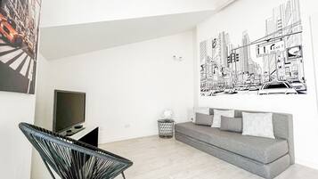 Ein modernes Wohnzimmer mit grauem Sofa, schwarzem Sessel und einer großen Wandmalerei mit Stadtansicht.