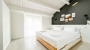 Ein modernes Schlafzimmer mit einem hölzernen Bett, weißer Bettwäsche, einem großen Fenster und einer dunklen Wand mit gerahmten Bildern.