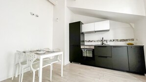 Una cocina compacta con armarios negros, una encimera blanca y un comedor con sillas y mesa blancos.