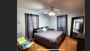 Un dormitorio con cama, una silla, un ventilador de techo y un espejo.