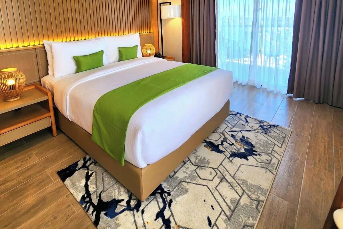 Habitación de hotel con una cama grande, paneles de madera, un equipo de aire acondicionado, una lámpara de noche y vistas por la ventana.