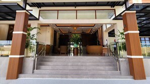 Una entrada de hotel moderna con techo de cristal, una escalera que conduce a la recepción y vistas de los edificios circundantes.