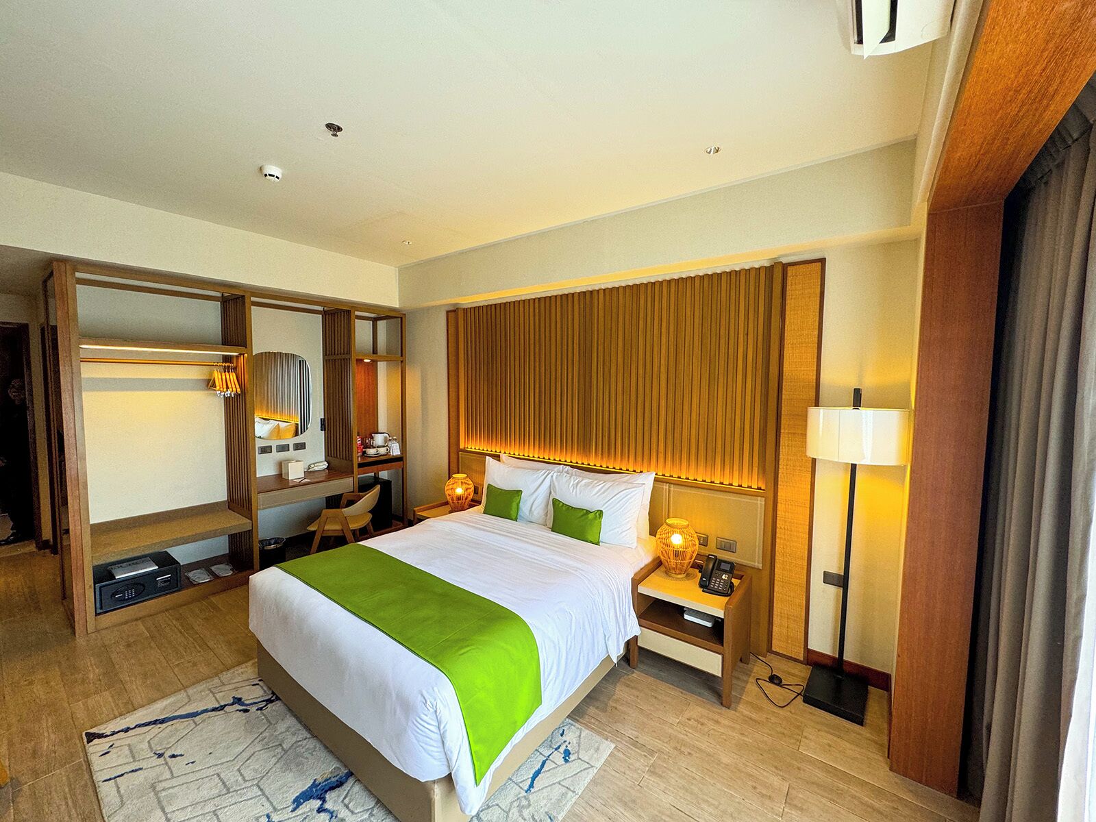 Une chambre d’hôtel comprenant un lit, des tables de chevet, un bureau, une chaise, un miroir et une armoire.