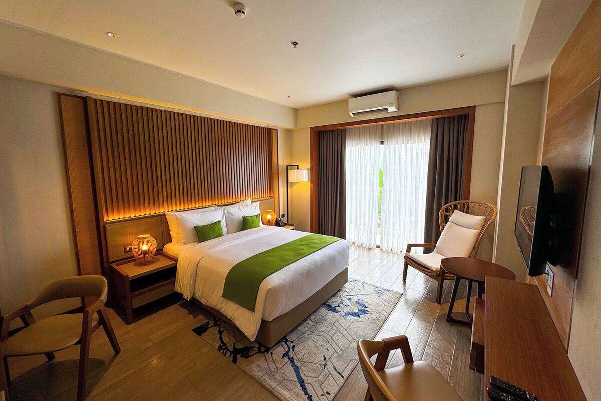 Habitación de hotel con una cama grande, un escritorio, una silla, un televisor y una ventana con cortinas.