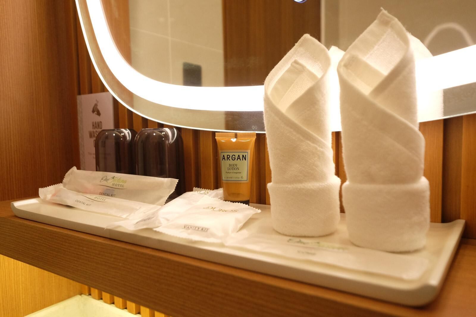 A hotel bathroom vanity with a mirror, toiletries, and a towel rack.