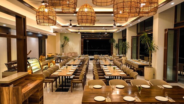 Un restaurante con varias mesas, lámparas de techo de mimbre y ventanas grandes.